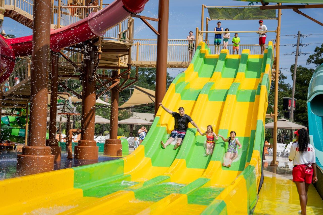 One adult and two children slide down a 3-lane multi-lane water slide at a water park